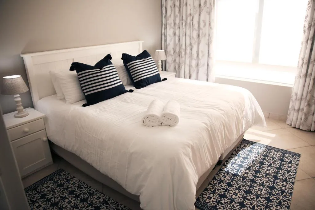 Bright bedroom with white bed, striped navy pillows, and folded towels