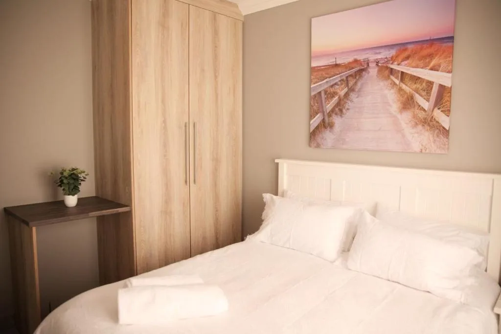 Bright bedroom with white bedding, wooden wardrobe, and coastal artwork