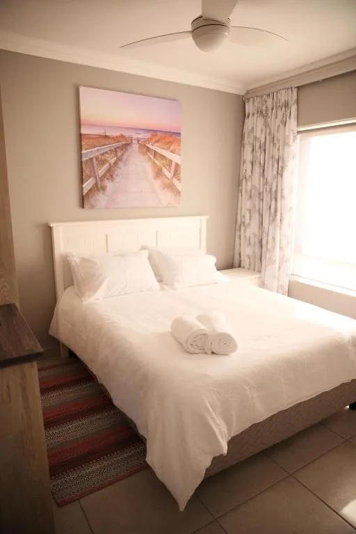 Bright bedroom with white bedding, ceiling fan, and landscape artwork on wall