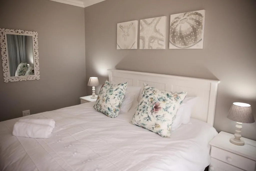 Spacious bedroom with white bed, floral pillows, and coastal wall art