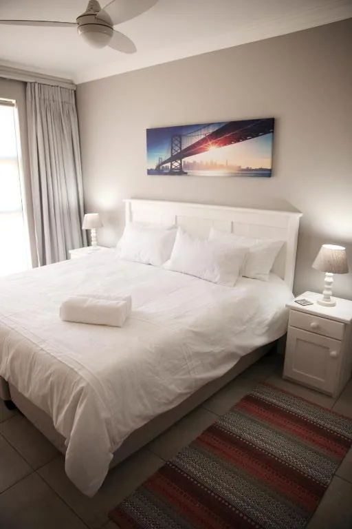 Bright bedroom with white bedding, bedside tables, and curtained window
