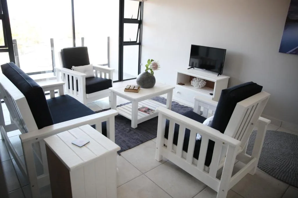 Modern living room with white furniture, black cushions, and flat-screen television