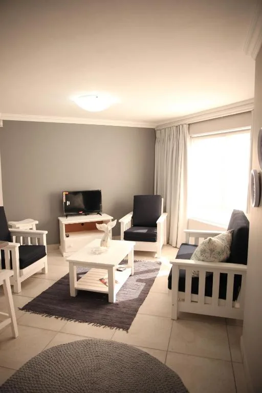 Bright lounge with white furniture, TV, and garden view through large windows