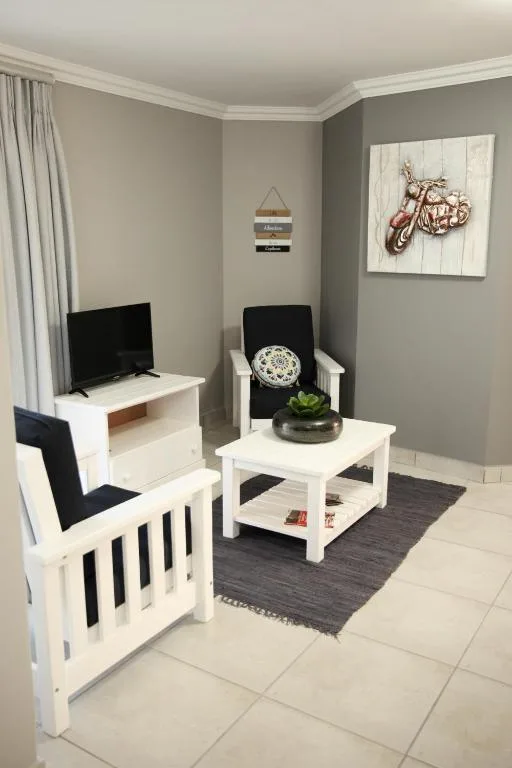 Modern lounge with white furniture, flat-screen TV, and grey walls
