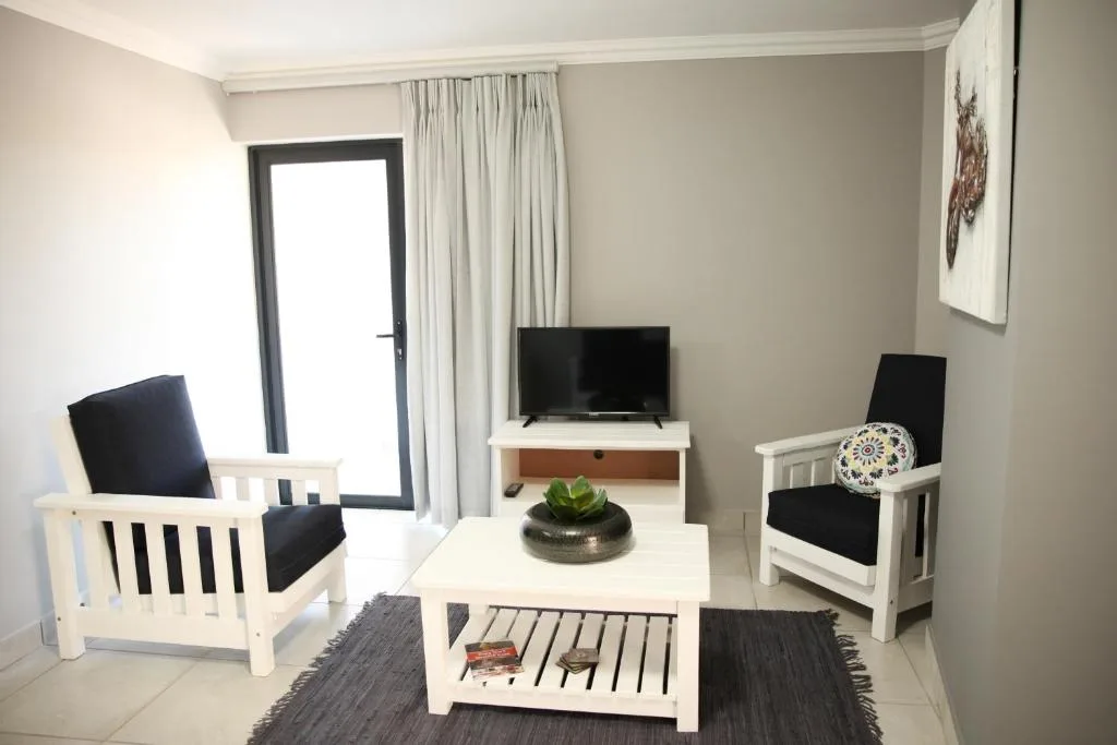Modern lounge with white armchairs, TV, and glass door access