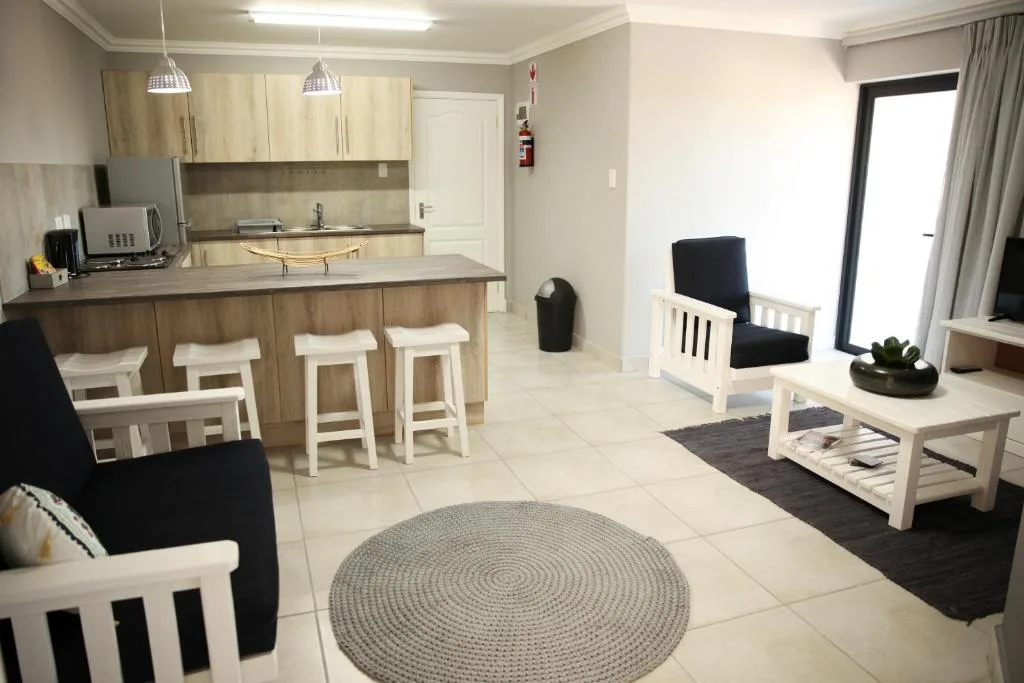 Open-plan lounge with black armchairs, round grey rug, and kitchen counter visible