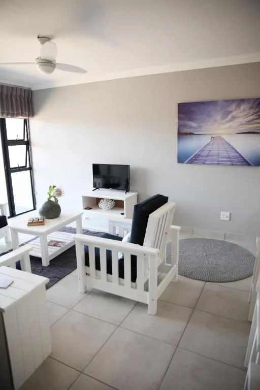 Bright living room with white furniture, TV, and scenic wall art