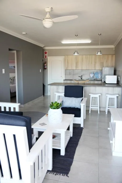 Open-plan living room with kitchen, white bar stools, ceiling fan, pendant lights