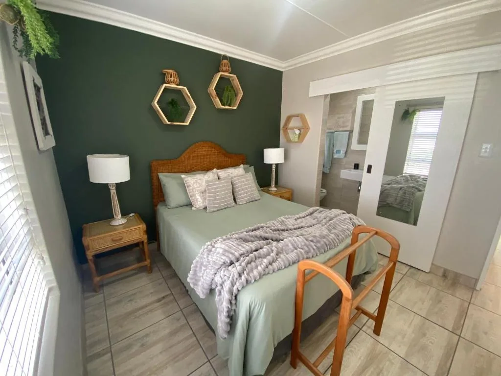 Spacious bedroom with queen bed, green accent wall, wooden nightstands, and ensuite access