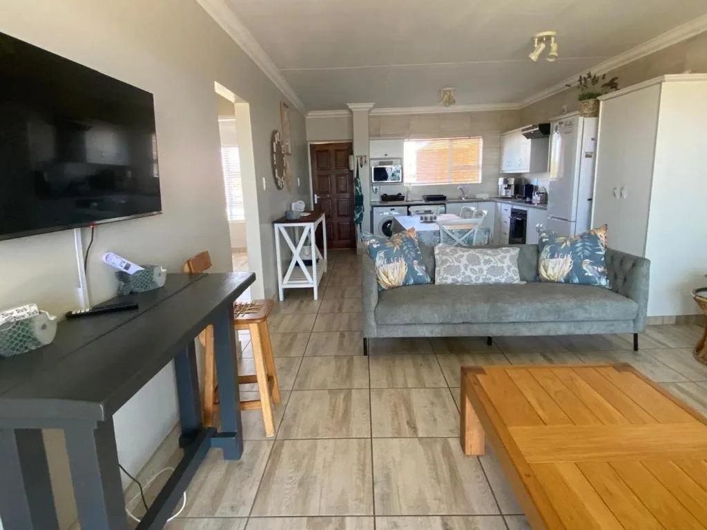 Open-plan living area with gray sofa, TV, and kitchen visible in background