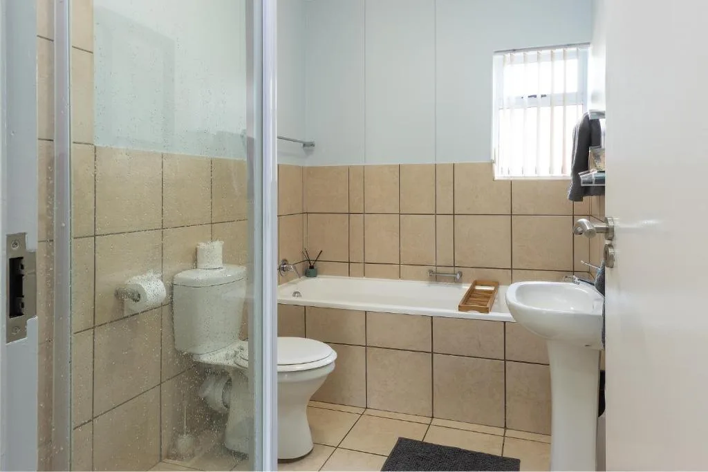 Bathroom with beige tile walls, white vanity sink, toilet, and bathtub with shower