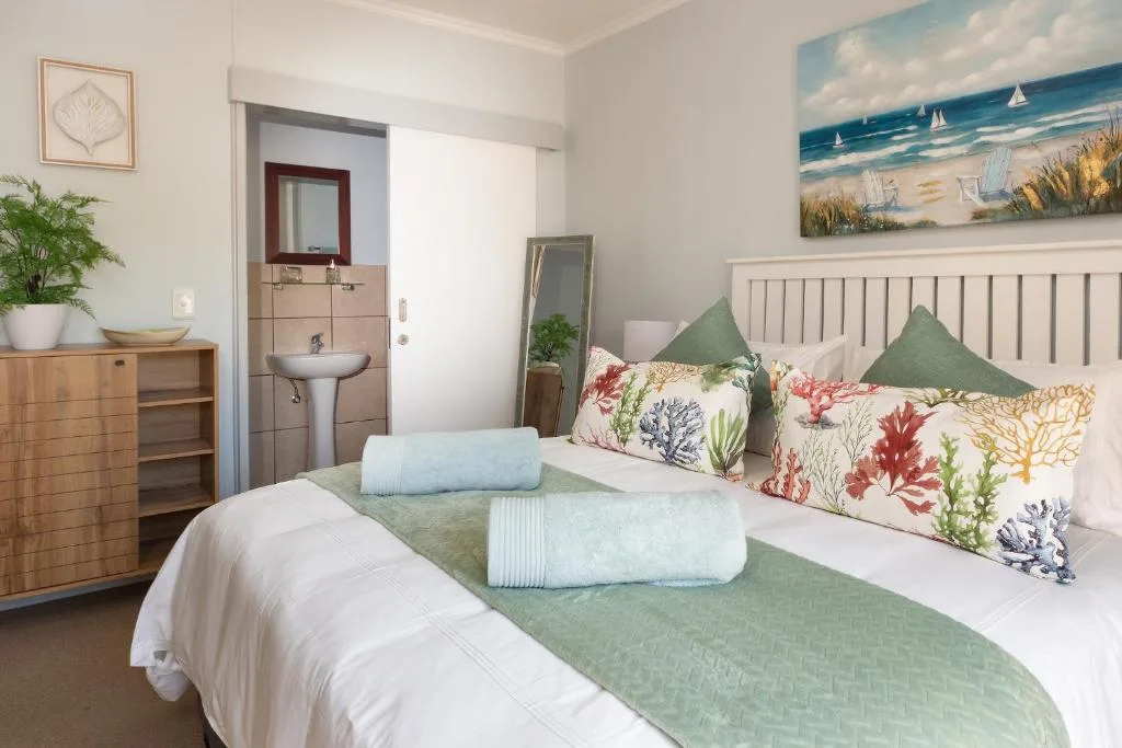 Bright bedroom with white bed, colorful coral patterned pillows, green accents