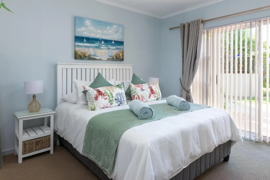 Bright bedroom with white bed, colorful floral pillows, and garden view