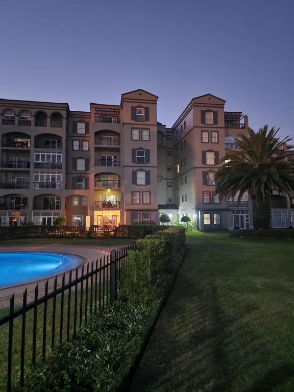 Multi-story apartment building with illuminated pool and manicured lawn at dusk