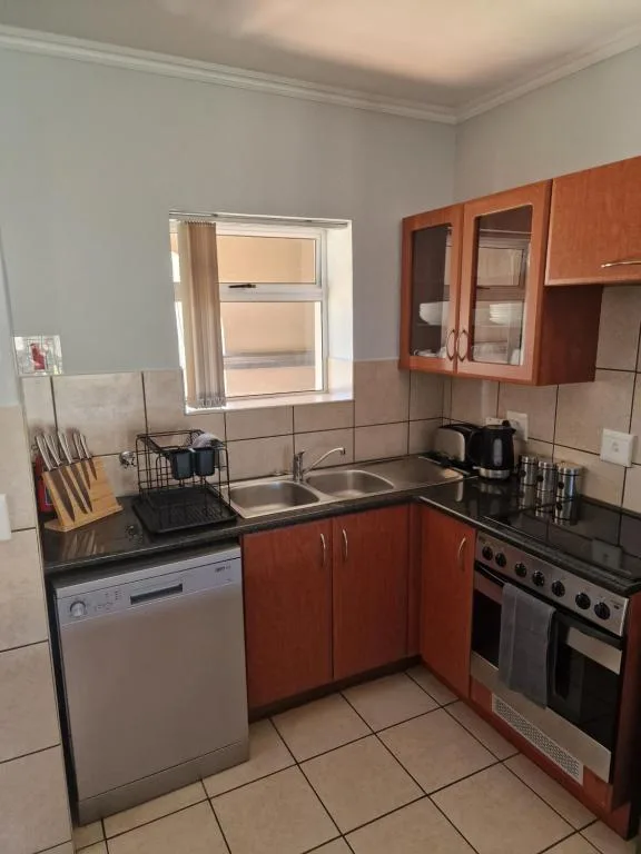 Compact kitchen with red cabinetry, stove, sink, and dishwasher