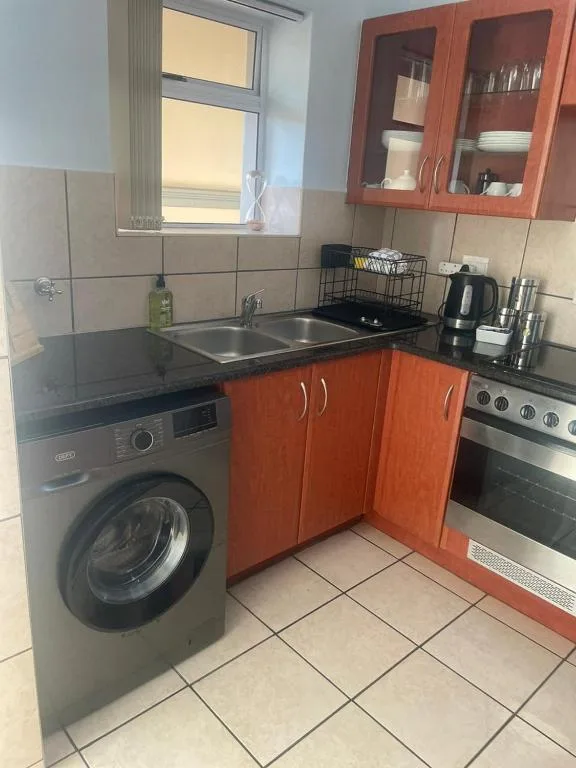 Compact kitchen with red cabinetry, stove, washing machine, and sink