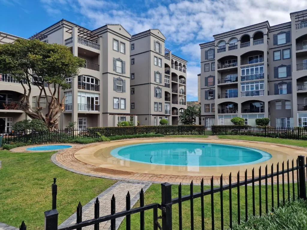Turquoise circular swimming pool surrounded by manicured lawn and apartment buildings