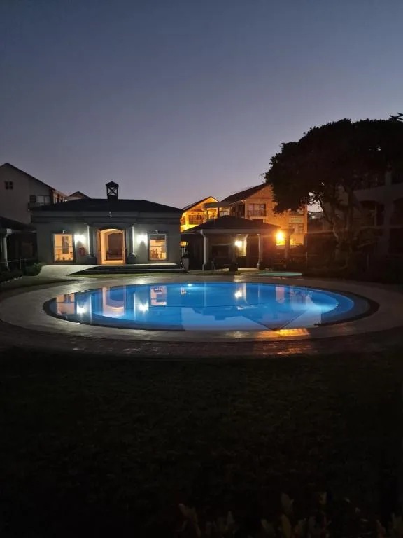 Illuminated oval swimming pool at dusk with lit house and deck behind