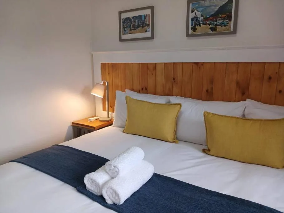 Spacious bedroom with wooden headboard, yellow pillows, and rolled towels
