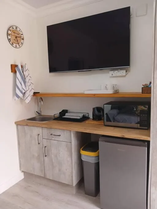 Compact kitchenette with wooden countertop, wall-mounted TV, and clock