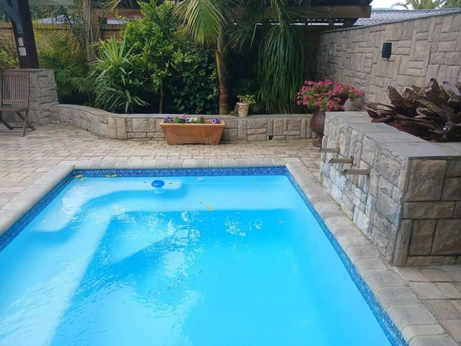 Bright blue rectangular swimming pool in landscaped courtyard with stone walls