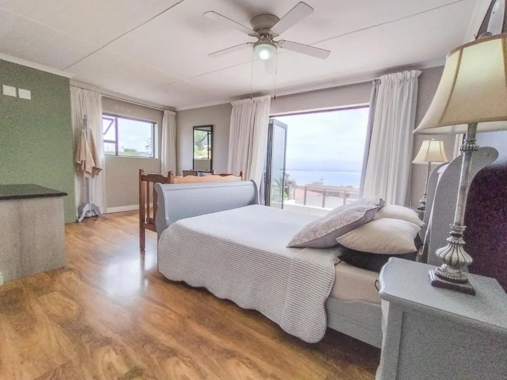 Spacious bedroom with double bed, ocean view through glass doors, ceiling fan