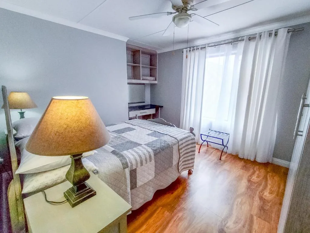 Bright bedroom with twin beds, wooden floors, and large windows with white curtains