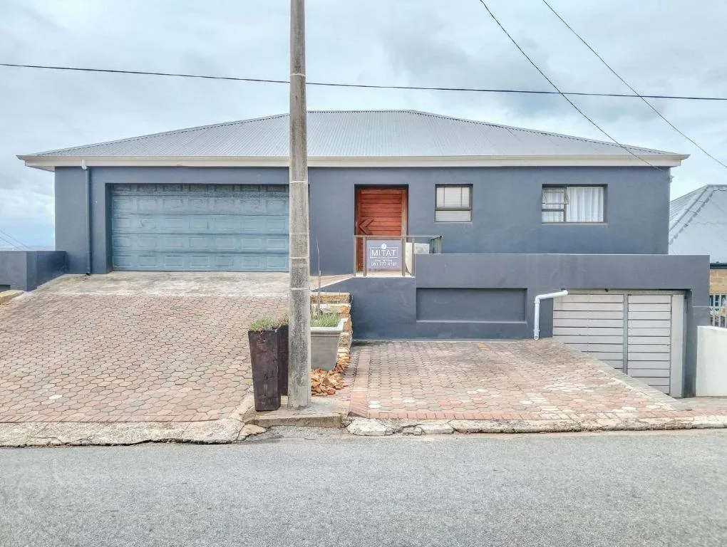 Modern blue-grey house with garage, brick driveway, and red entrance door