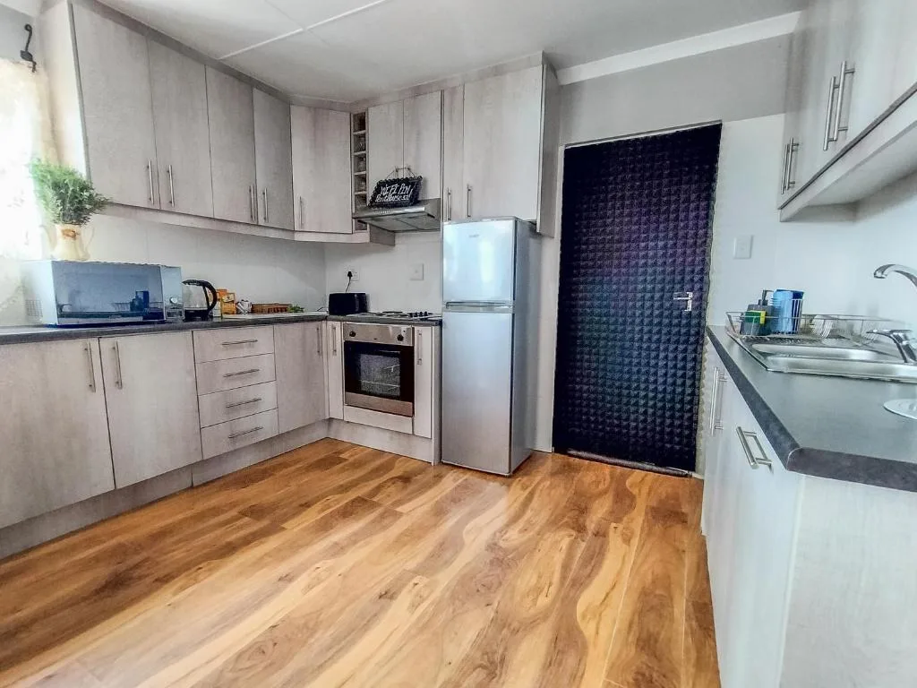 Modern kitchen with light wood cabinetry, stainless steel appliances, and wooden flooring