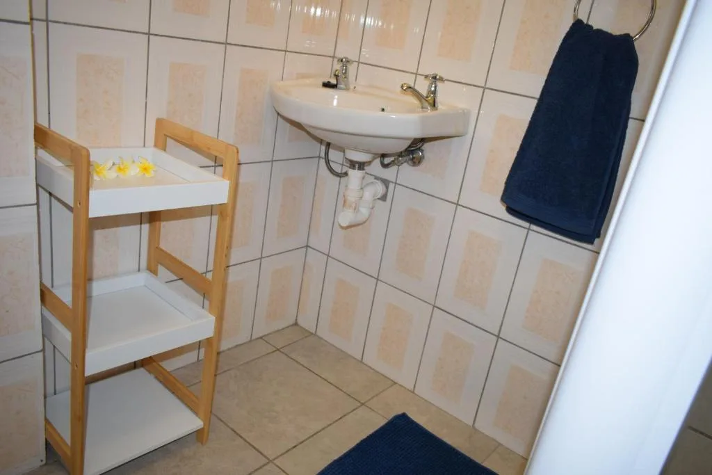 Clean bathroom with white double sink, wooden shelving unit, and navy towel