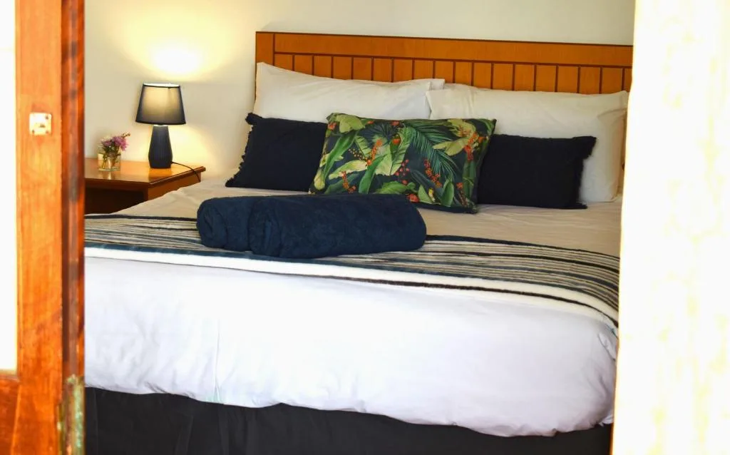 Wooden bed with white linens, decorative pillows, and bedside lamp in warm bedroom