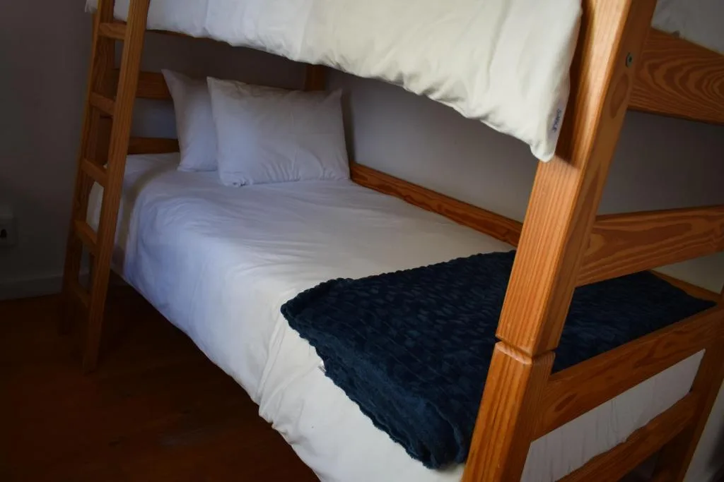 Wooden bunk bed with white linens and dark throw blanket