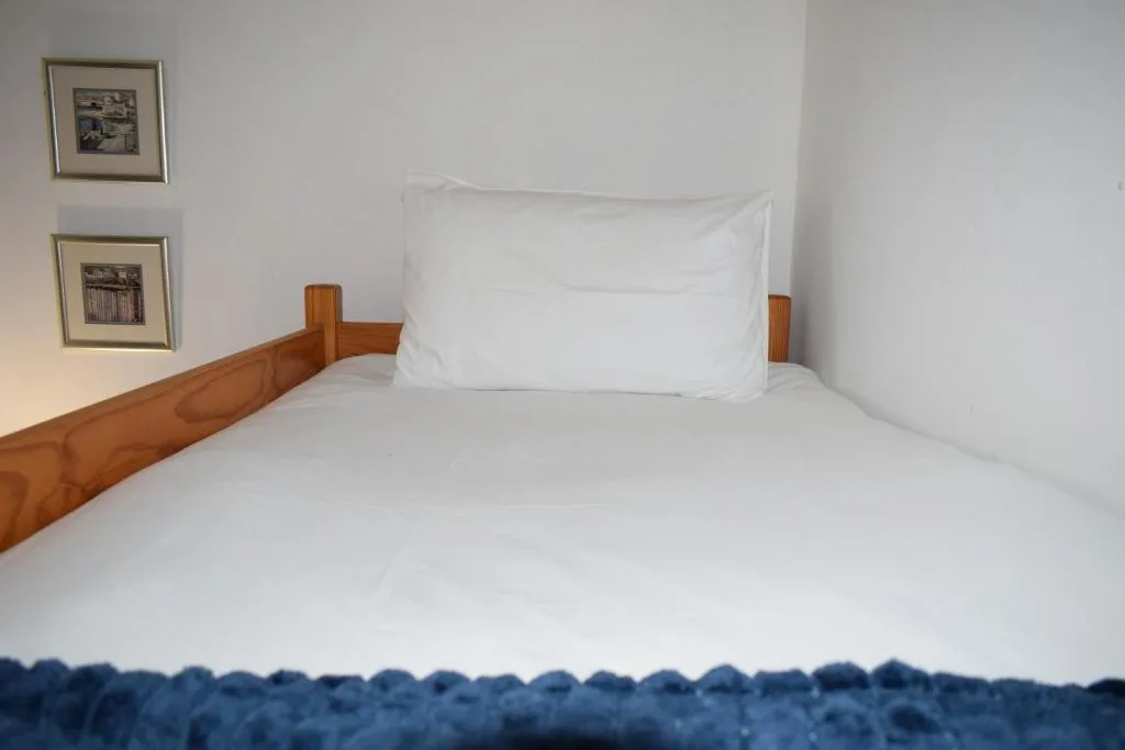 Clean bed with white linens and wooden headboard in bright bedroom