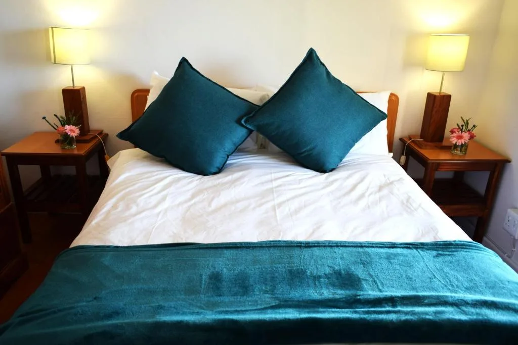 Master bedroom with white linens, teal cushions, wooden nightstands, matching lamps