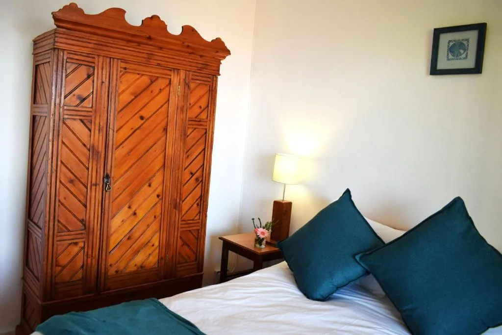 Bedroom with bed, teal pillows, wooden wardrobe, and bedside lamp