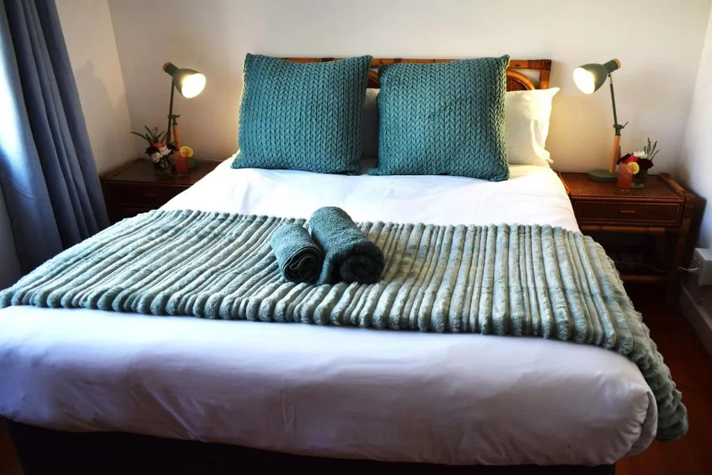 Double bed with teal pillows, white linens, and rolled towels at foot
