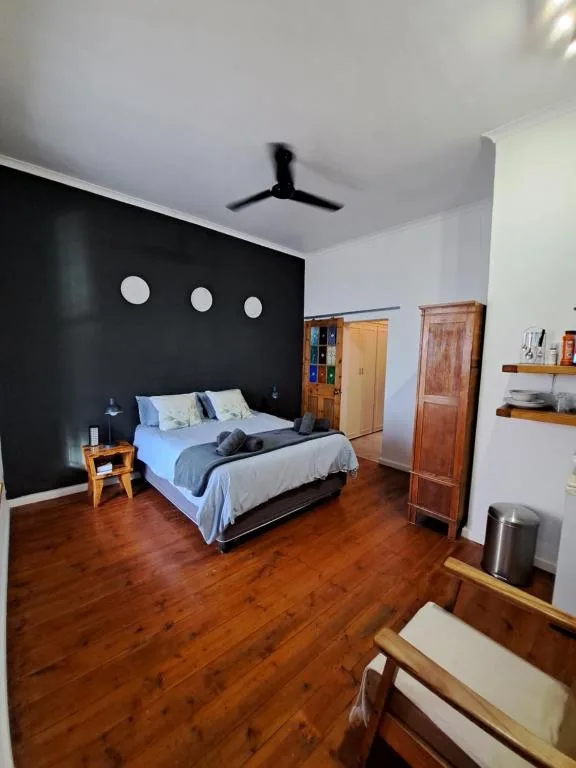 Modern bedroom with black accent wall, queen bed, wooden floors, ceiling fan