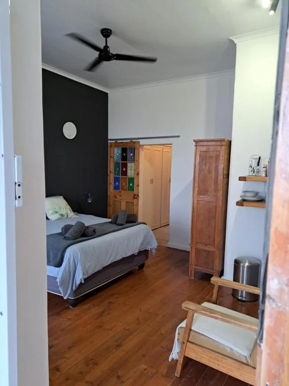 Bright bedroom with single bed, black accent wall, wooden wardrobes, ceiling fan