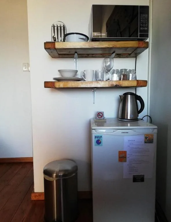 Compact kitchen corner with microwave, refrigerator, and wooden shelving