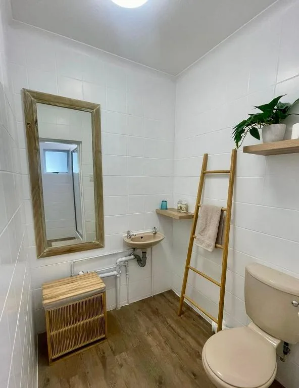 Clean bathroom with white tiles, wooden mirror frame, and toilet