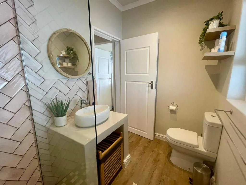 Modern bathroom with herringbone tile, round mirror, vessel sink, and toilet