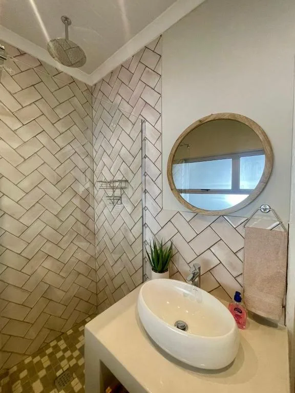 Modern bathroom with herringbone tile shower, round mirror, and vessel sink
