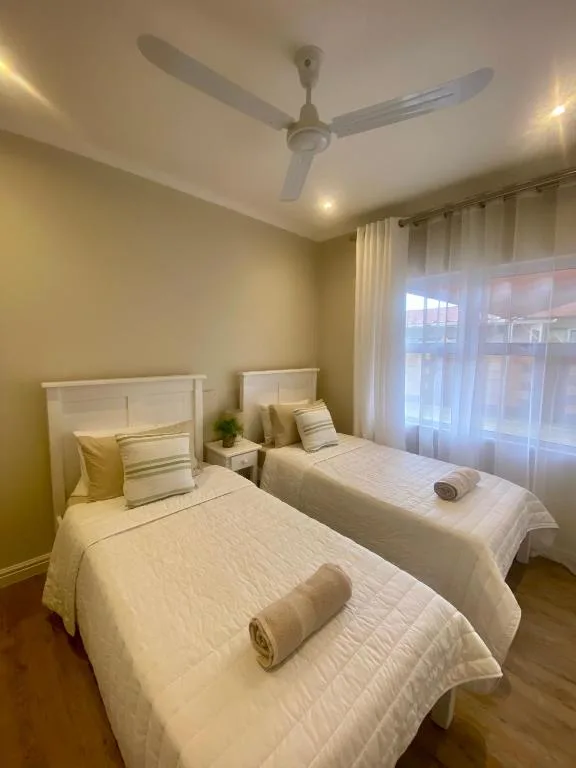 Bright bedroom with two single beds, white headboards, and ceiling fan
