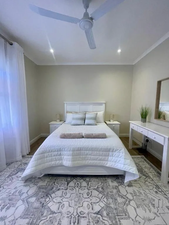 Bright bedroom with white bed, nightstands, and modern vanity mirror