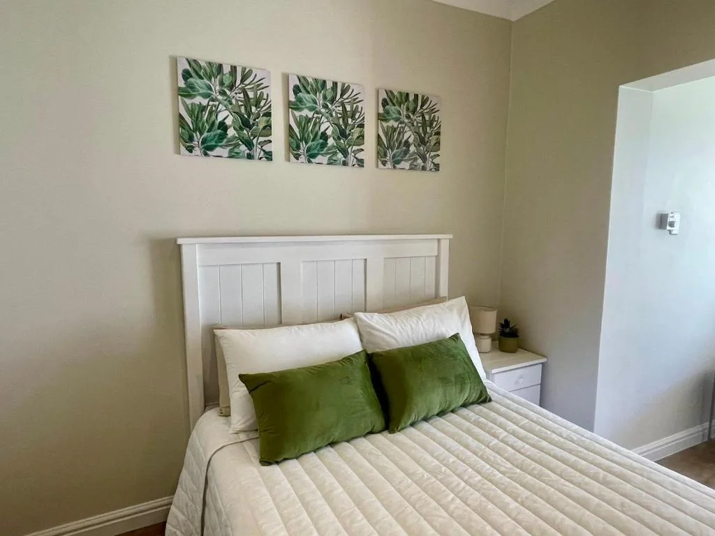Bright bedroom with white headboard, green pillows, botanical wall art