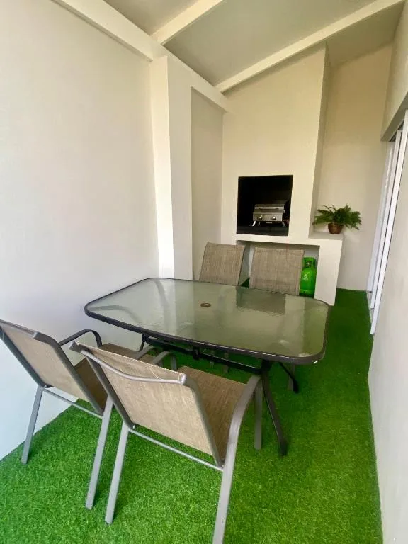 Modern dining area with glass table and four beige chairs on artificial turf