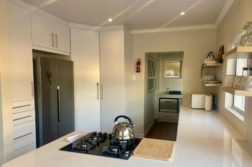 Modern kitchen with white cabinetry, gas cooktop, stainless steel fridge, and open shelving