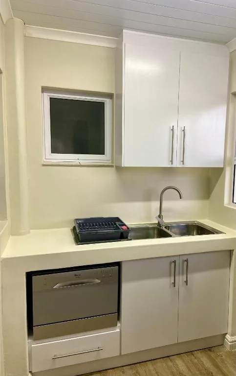 Compact kitchen with white cabinetry, stainless steel sink and appliances