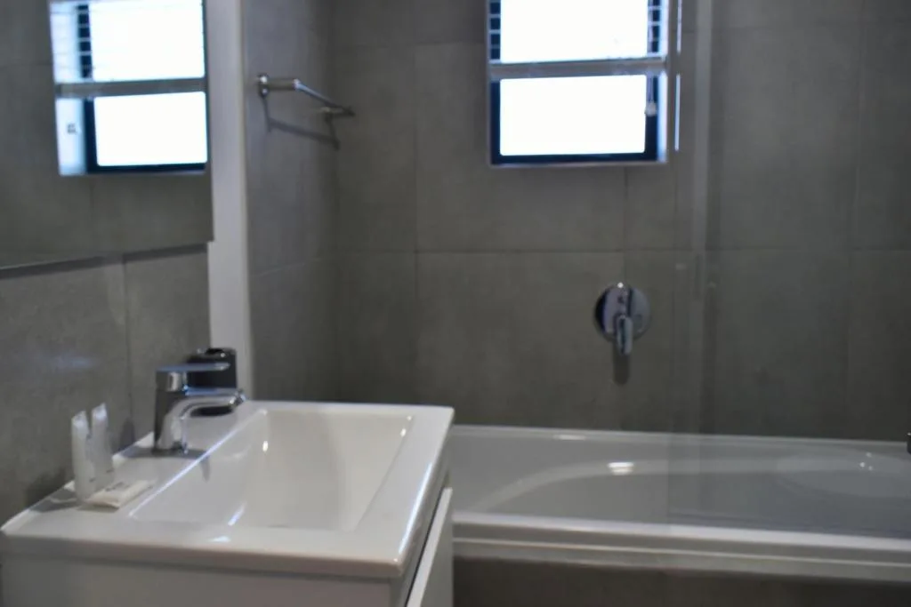 Modern bathroom with white basin, bathtub, and tiled walls with windows