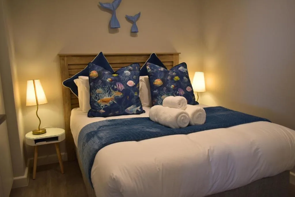 Cozy bedroom with ocean-themed pillows, white bedding, and warm bedside lighting